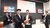 Academic in cap and gown hands red diploma to smiling graduate in suit at ceremony