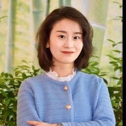 Woman in blue cardigan stands with arms crossed before bamboo backdrop