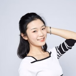 Young woman in white striped top smiles with hand behind head against light gray background.